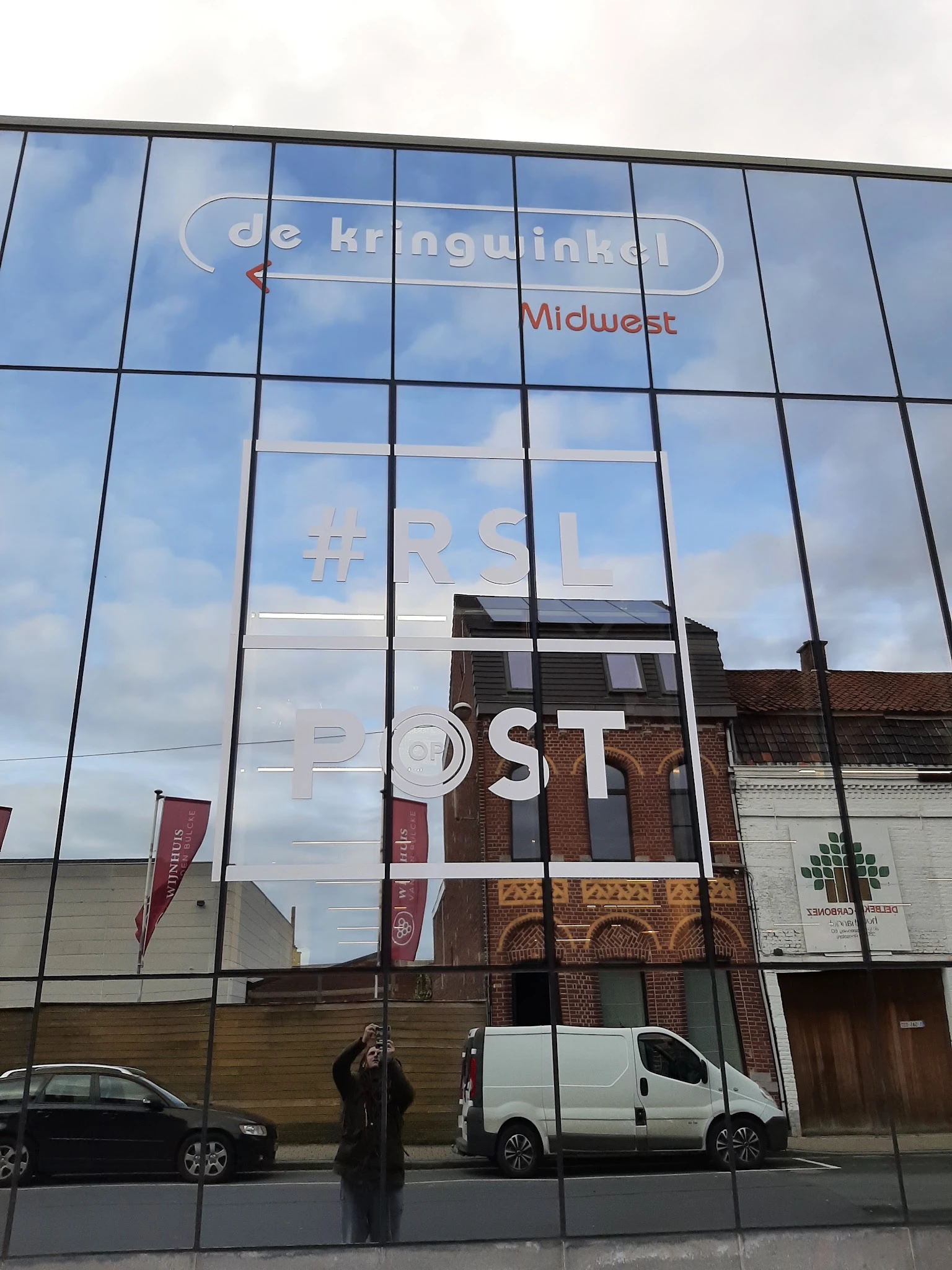 Glazen gevel van kringloopwinkel met reflectie van omgeving en witte letters op raam