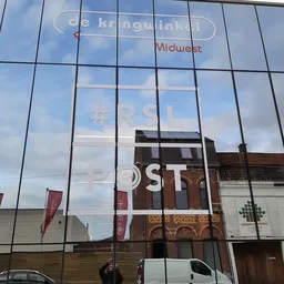 Glazen gevel van kringloopwinkel met reflectie van omgeving en witte letters op raam