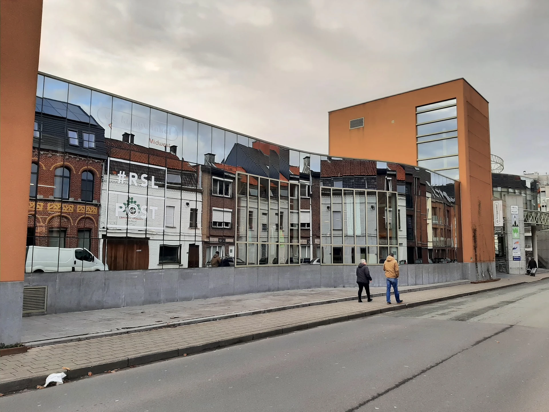 Voorgevel van kringloopwinkel aan Noordlaan met moderne glazen uitbouw en betonnen afsluiting, twee personen op straat