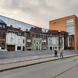 Voorgevel van kringloopwinkel aan Noordlaan met moderne glazen uitbouw en betonnen afsluiting, twee personen op straat