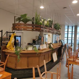 Houten baliebalie met hangplanten en gele decoratie, stoelen aan tafels in lunchruimte
