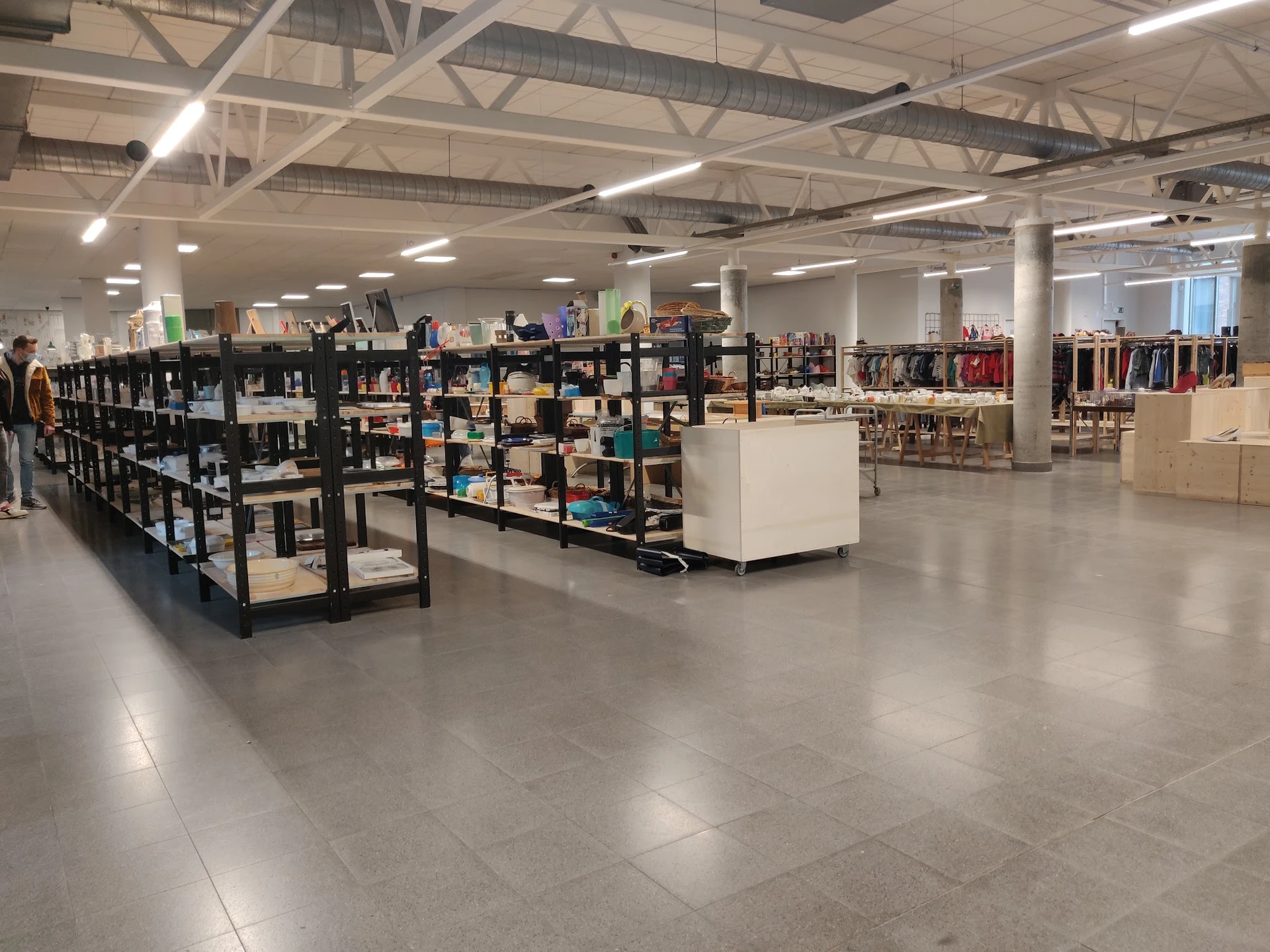 Ruim winkelbinnenruimte met zwarte stellingen vol spullen, witte display-elementen en kleding op hangers in de achtergrond