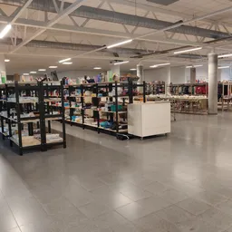 Ruim winkelbinnenruimte met zwarte stellingen vol spullen, witte display-elementen en kleding op hangers in de achtergrond