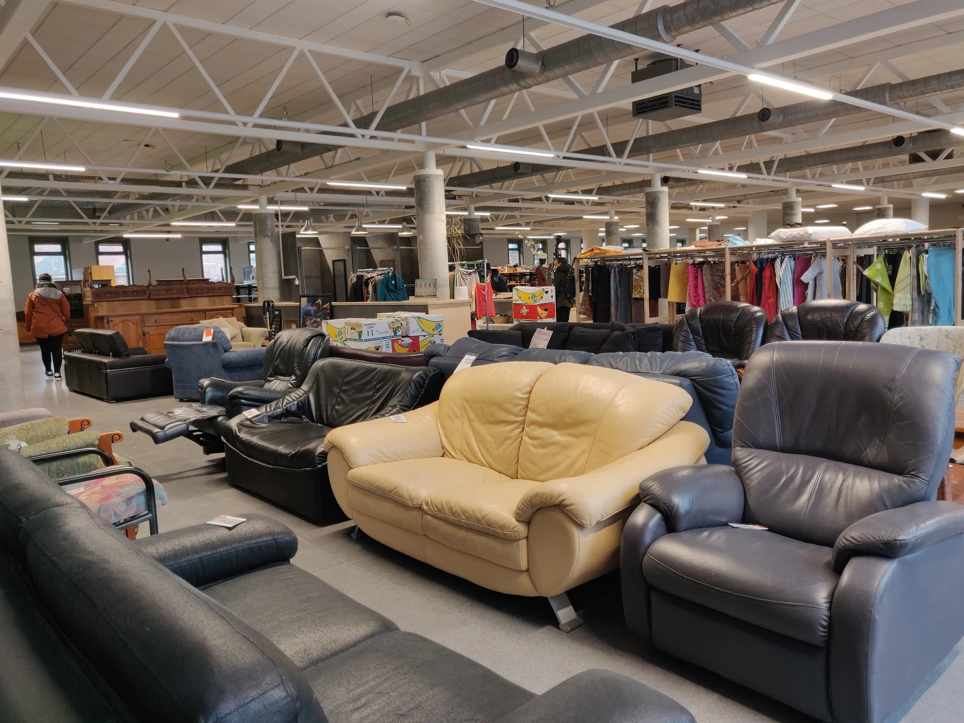 Winkelvloer met diverse gebruikt meubels, waaronder gele en zwarte fauteuils, kledingrekken op de achtergrond en winkelkolomm