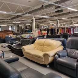 Winkelvloer met diverse gebruikt meubels, waaronder gele en zwarte fauteuils, kledingrekken op de achtergrond en winkelkolomm