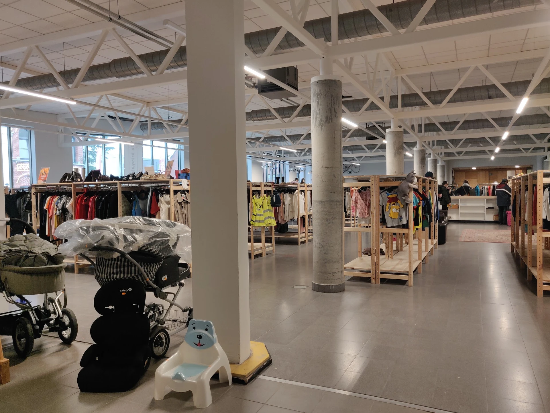 Ruim winkelinterieur met kledingrekken, stellingen en diverse spullen, waaronder kinderwagens op de vloer