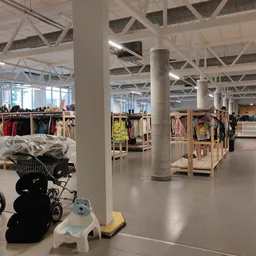 Ruim winkelinterieur met kledingrekken, stellingen en diverse spullen, waaronder kinderwagens op de vloer
