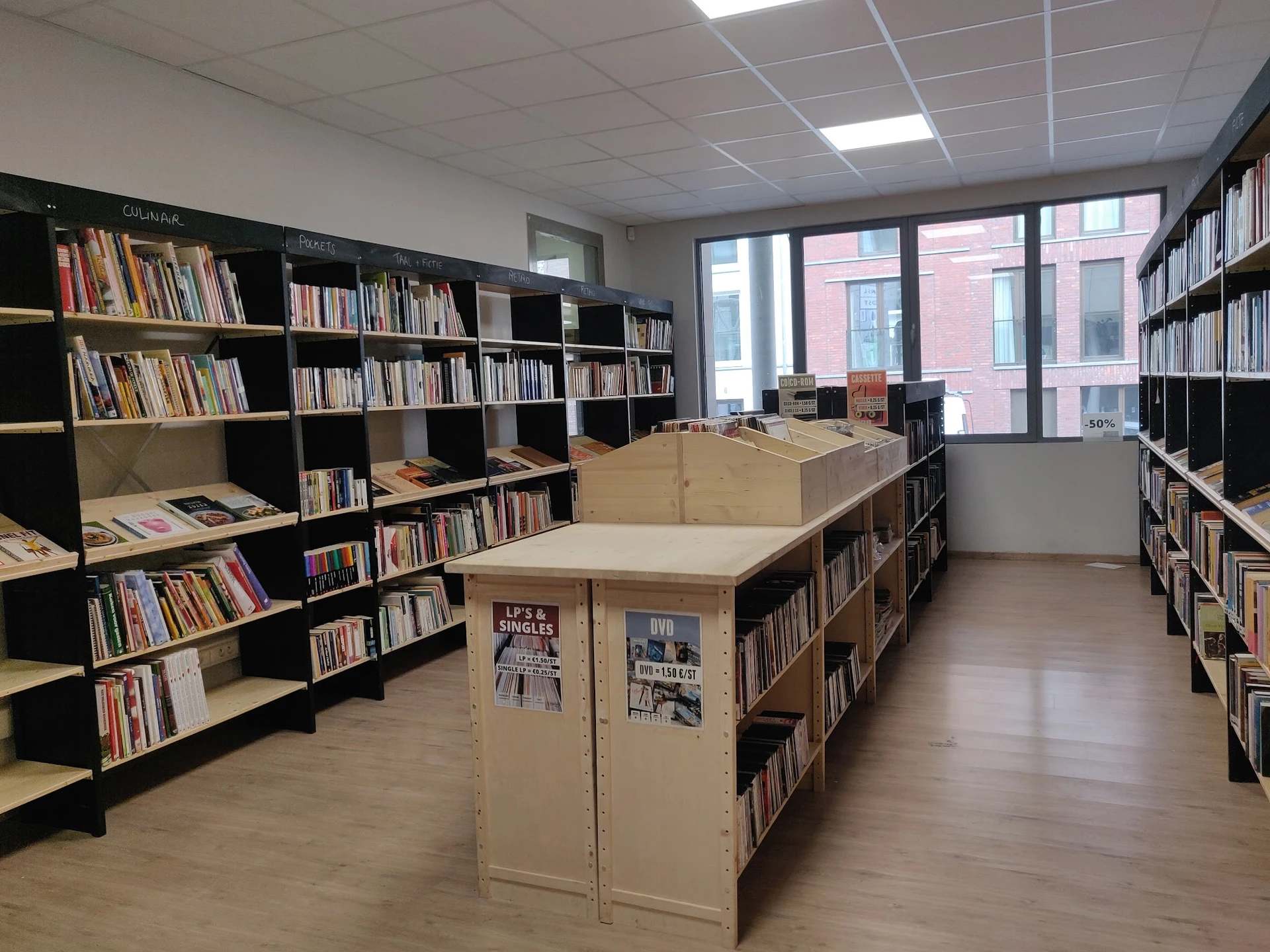 Boekenrekken en stellingen in een kringloopwinkel met houten vloer en grote ramen