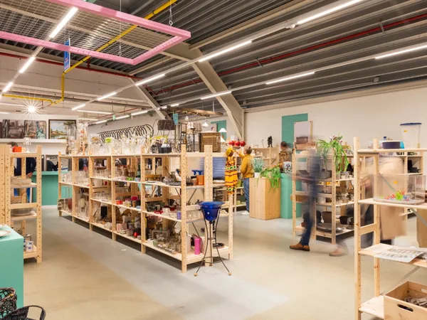 Ruime winkelruimte met houten stellingen vol spullen, moderne verlichting en groene accenten