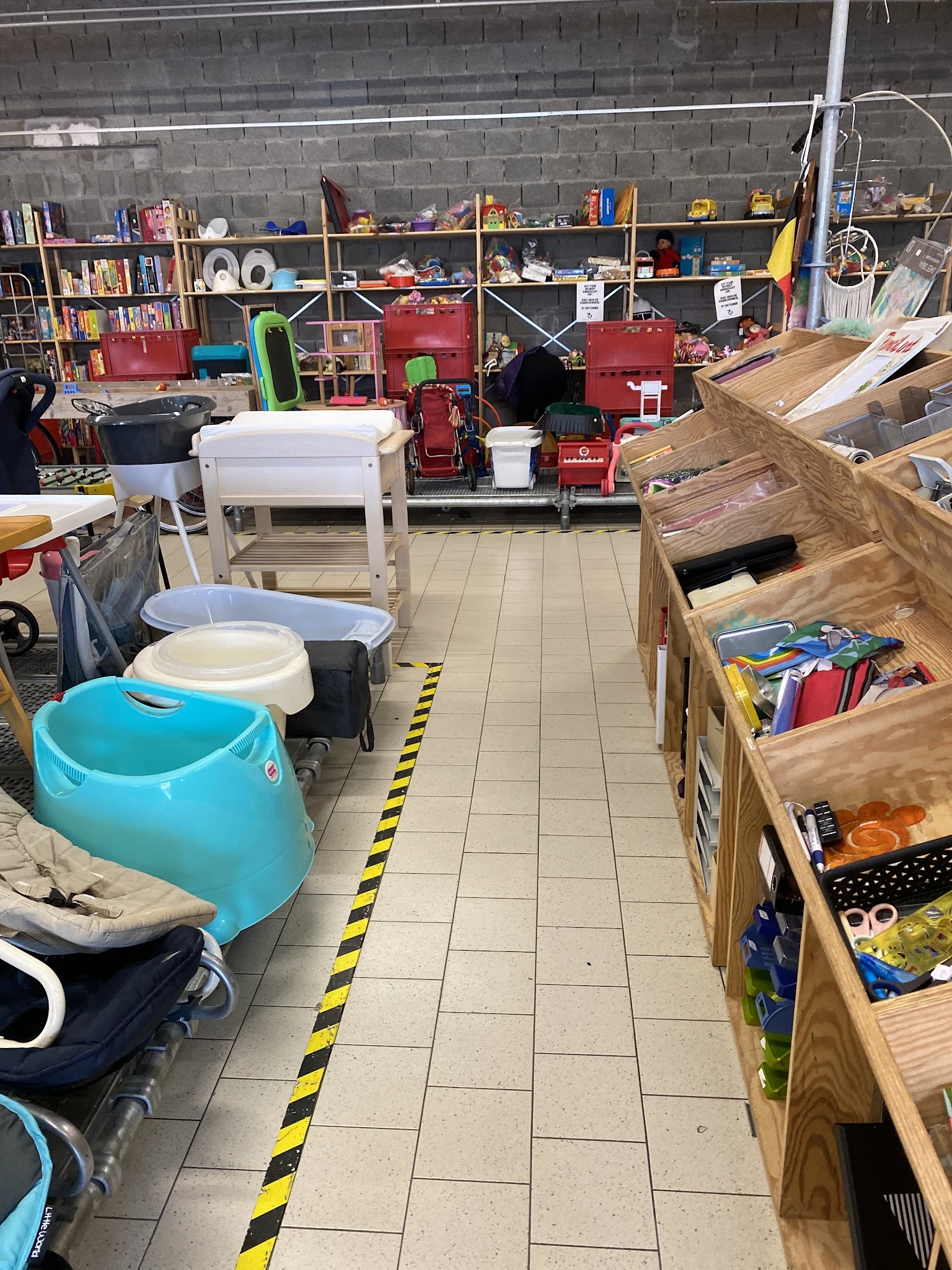 Winkelvloer met diverse artikelen: blauwe kinderbaden, witte manden, houten boxen met speelgoed en boeken, rode meubels op ac