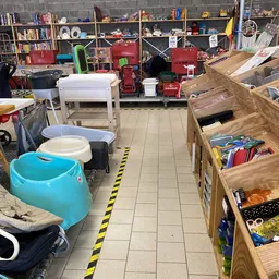 Winkelvloer met diverse artikelen: blauwe kinderbaden, witte manden, houten boxen met speelgoed en boeken, rode meubels op ac