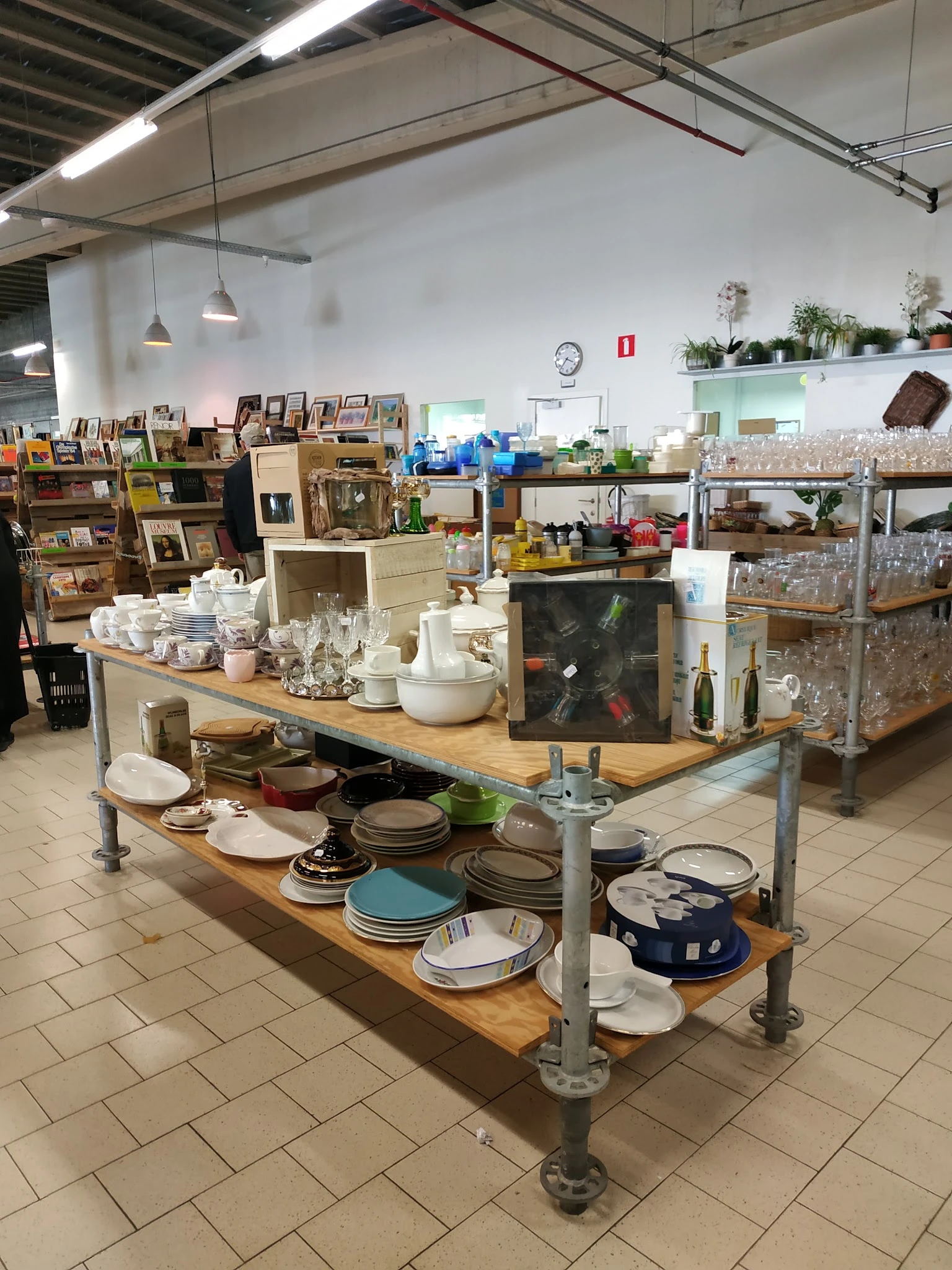 Tafel met uitgestalde serviesgoed, kopjes, borden en andere huishoudelijke artikelen in de kringloopwinkel