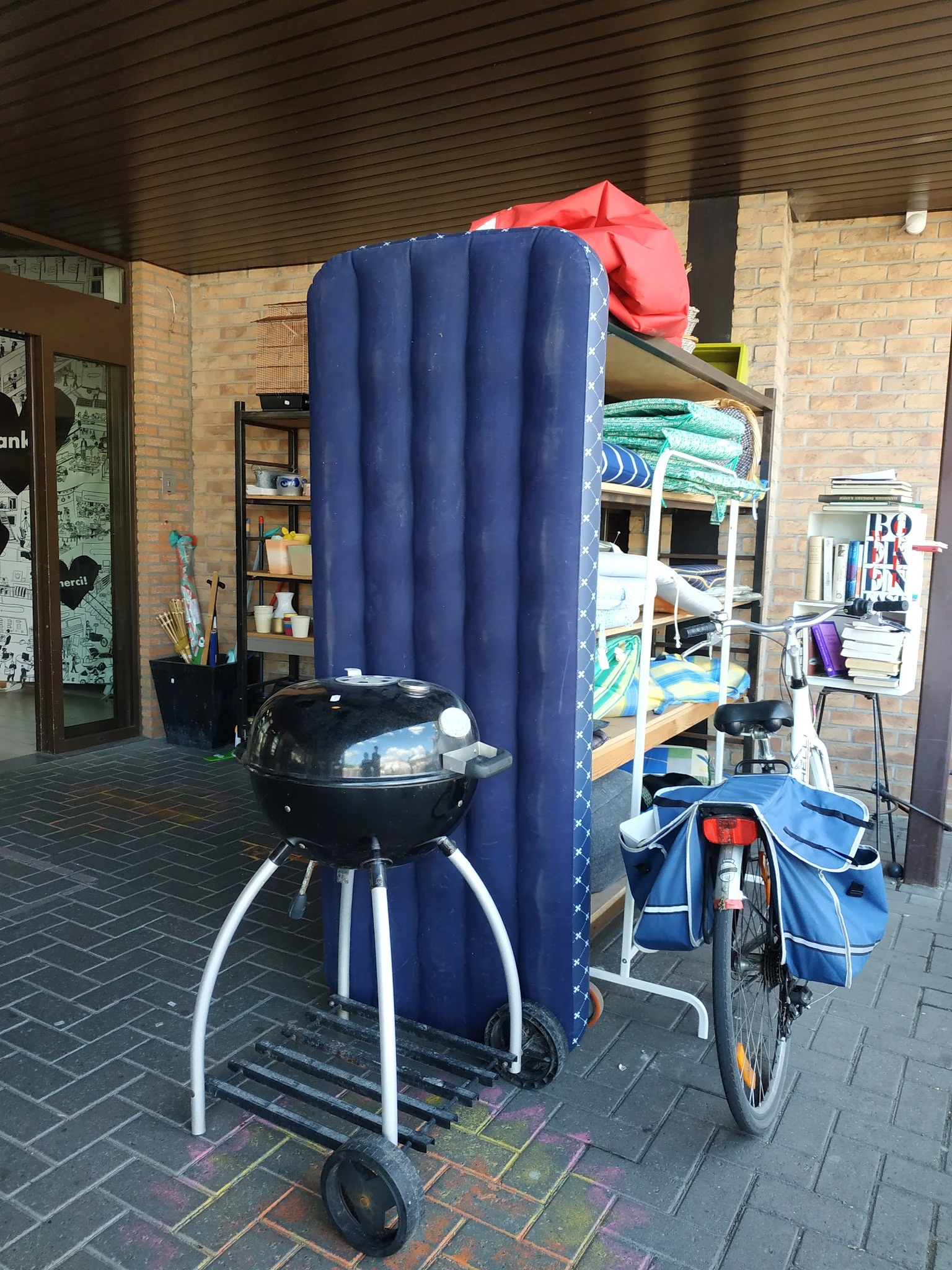 Winkelinterieur met blauwe gordijn, barbecue, stellingen met spullen en diverse tweedehandsartikelen