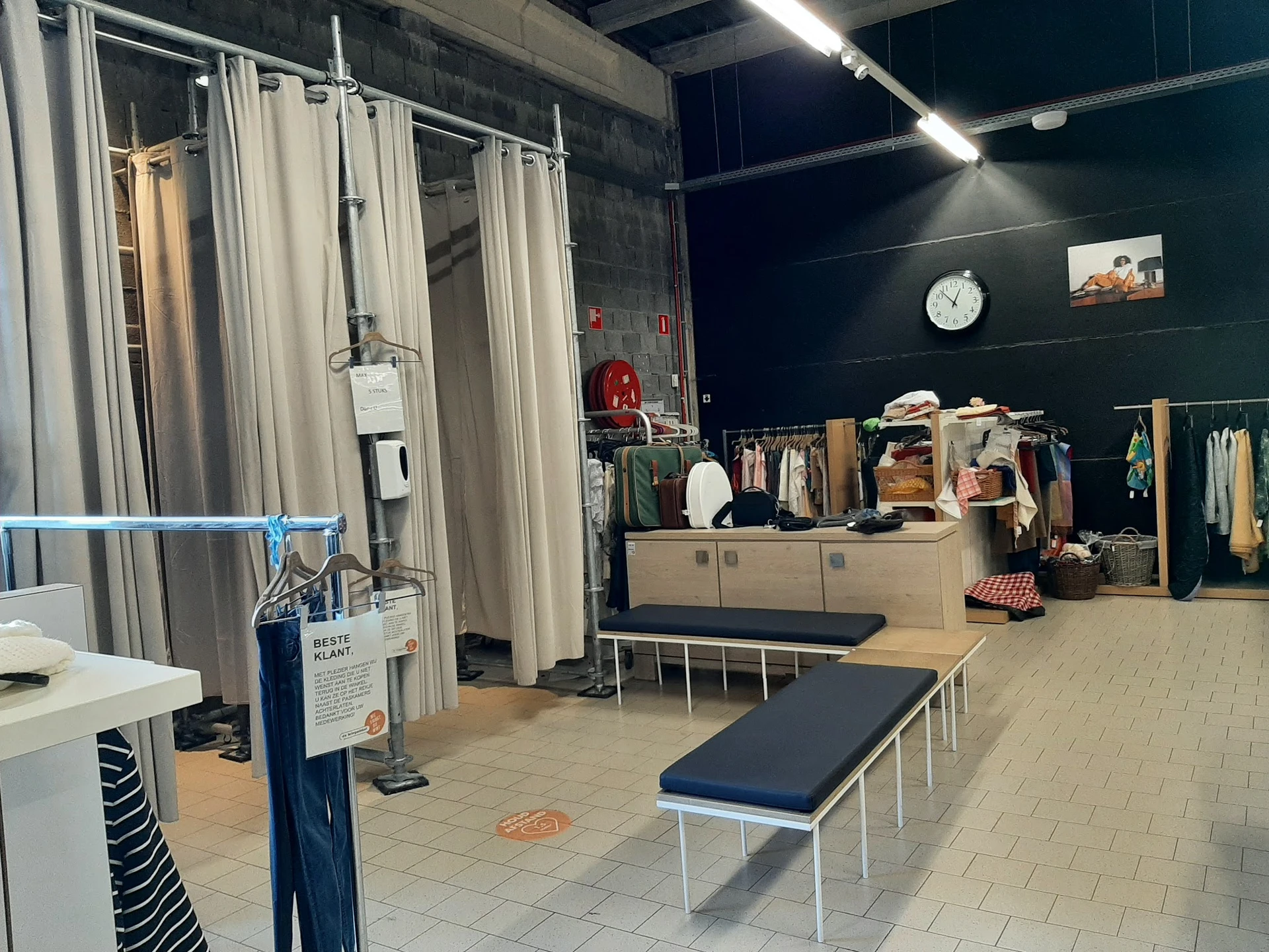 Winkelvloer met kledingrekken, paskamers met gordijnen en zitbank in kringloopwinkel