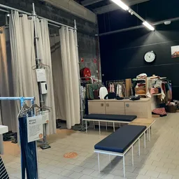 Winkelvloer met kledingrekken, paskamers met gordijnen en zitbank in kringloopwinkel