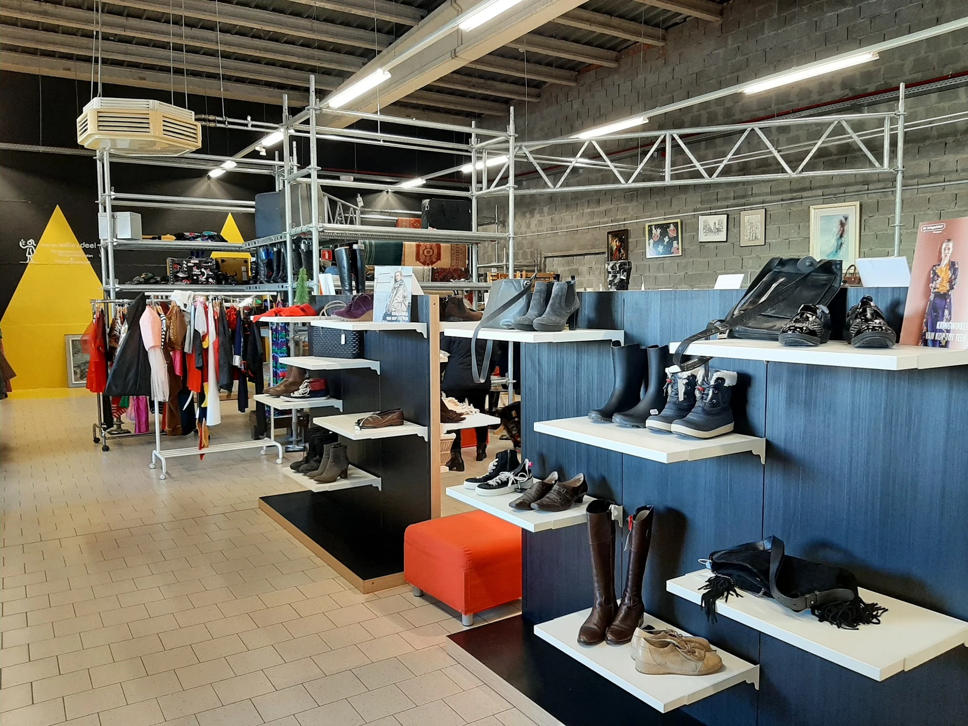 Winkelinterieur met blauwe stellingen vol schoenen en zwarte display-elementen, gele decoratie linksvoor, kledingrekken, held