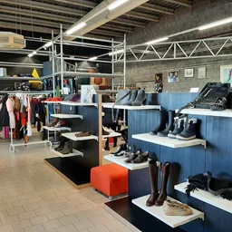 Winkelinterieur met blauwe stellingen vol schoenen en zwarte display-elementen, gele decoratie linksvoor, kledingrekken, held