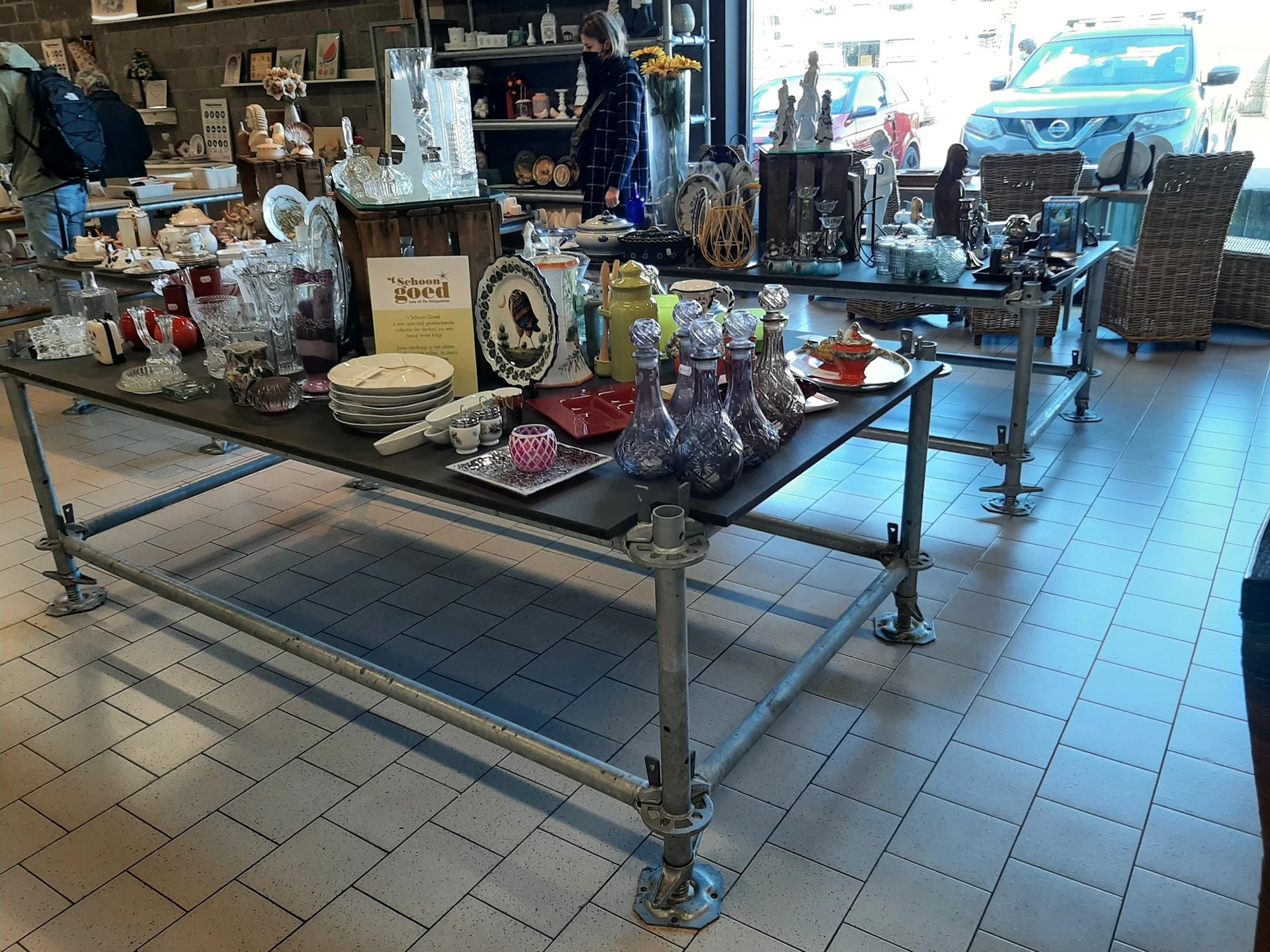 Uitgestalde huishoudspullen en decoratieve artikelen op tafels in de winkel, inclusief servies, beelden en overige tweedehand