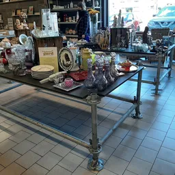 Uitgestalde huishoudspullen en decoratieve artikelen op tafels in de winkel, inclusief servies, beelden en overige tweedehand