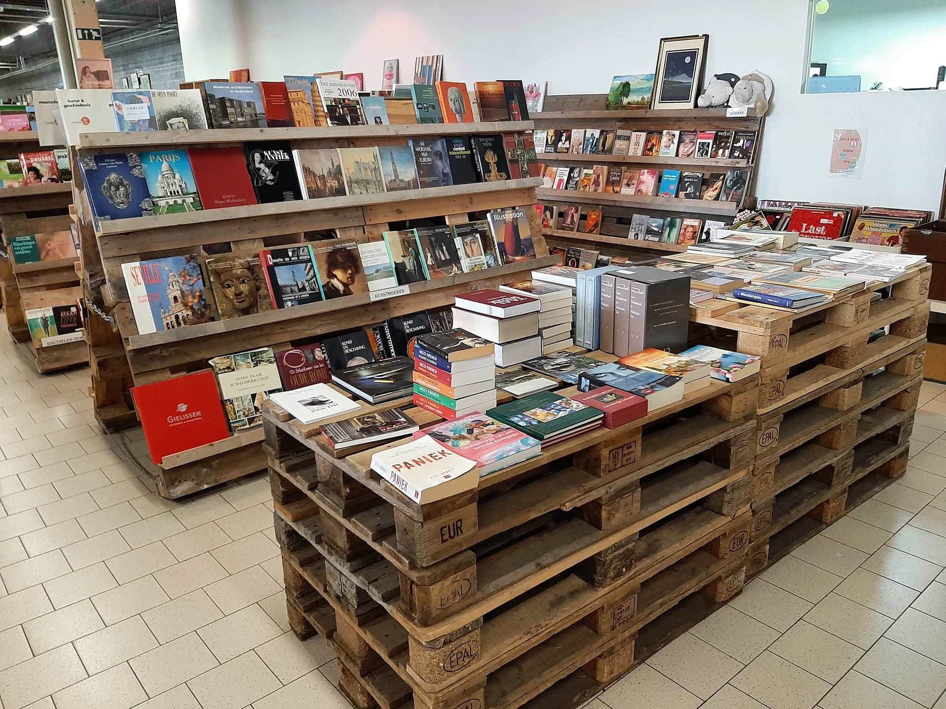 Boeken en media uitgestald op houten pallets en stellingen in een kringloopwinkel