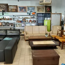 Winkelvloer met diverse meubels: zwarte leren bank, beige bank, houten stoelen, tafels en kasten met huishoudartikelen en dec