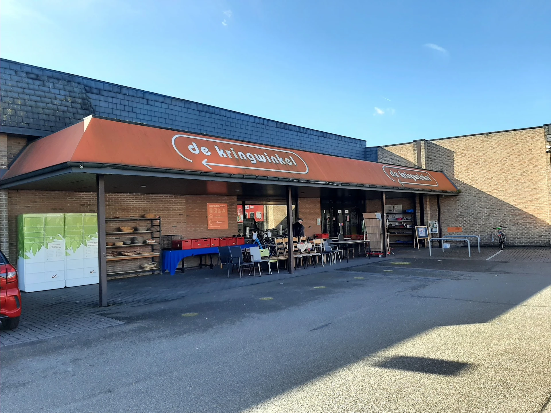 Voorgevel van kringloopwinkel met oranje luifel, winkelnaam zichtbaar, ingang en uitstalramen