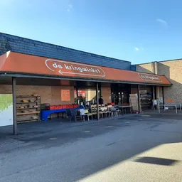Voorgevel van kringloopwinkel met oranje luifel, winkelnaam zichtbaar, ingang en uitstalramen