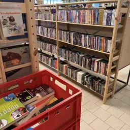 Houten stellingen met dvd's en blu-rays in een kringloopwinkel, rode plastic bak op de vloer