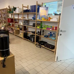 Winkelvloer met houten stellingen vol met diverse tweedehands artikelen, inclusief boeken, elektronica en huishoudartikelen