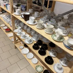 Houten stellingen met diverse serviesgoed: kopjes, schotels, kannen en borden in wit, grijs en zwart