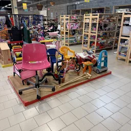 Uitgestalde kindermeubels en speelgoed op houten platform in kringloopwinkel