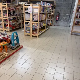 Winkelvloer met houten stellingen vol spullen, speelgoed op de grond, en rode brandblus aan de muur