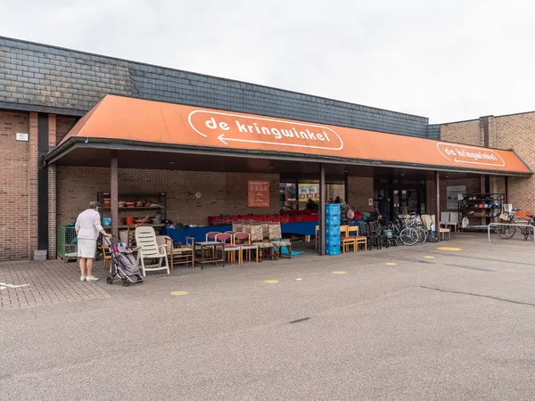 Voorgevel van kringloopwinkel met oranje luifel, uitgestalde meubels en fietsen op het terras