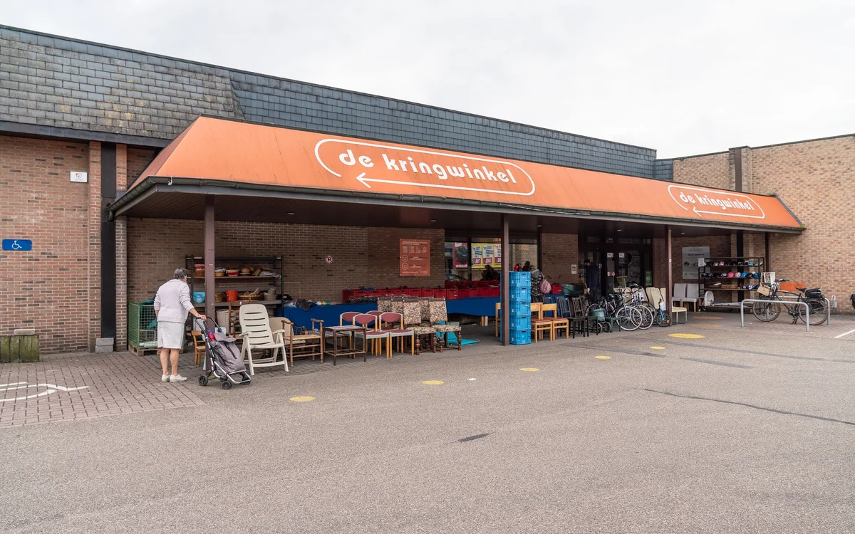 Voorgevel van kringloopwinkel met oranje luifel, uitgestalde meubels en fietsen op het terras