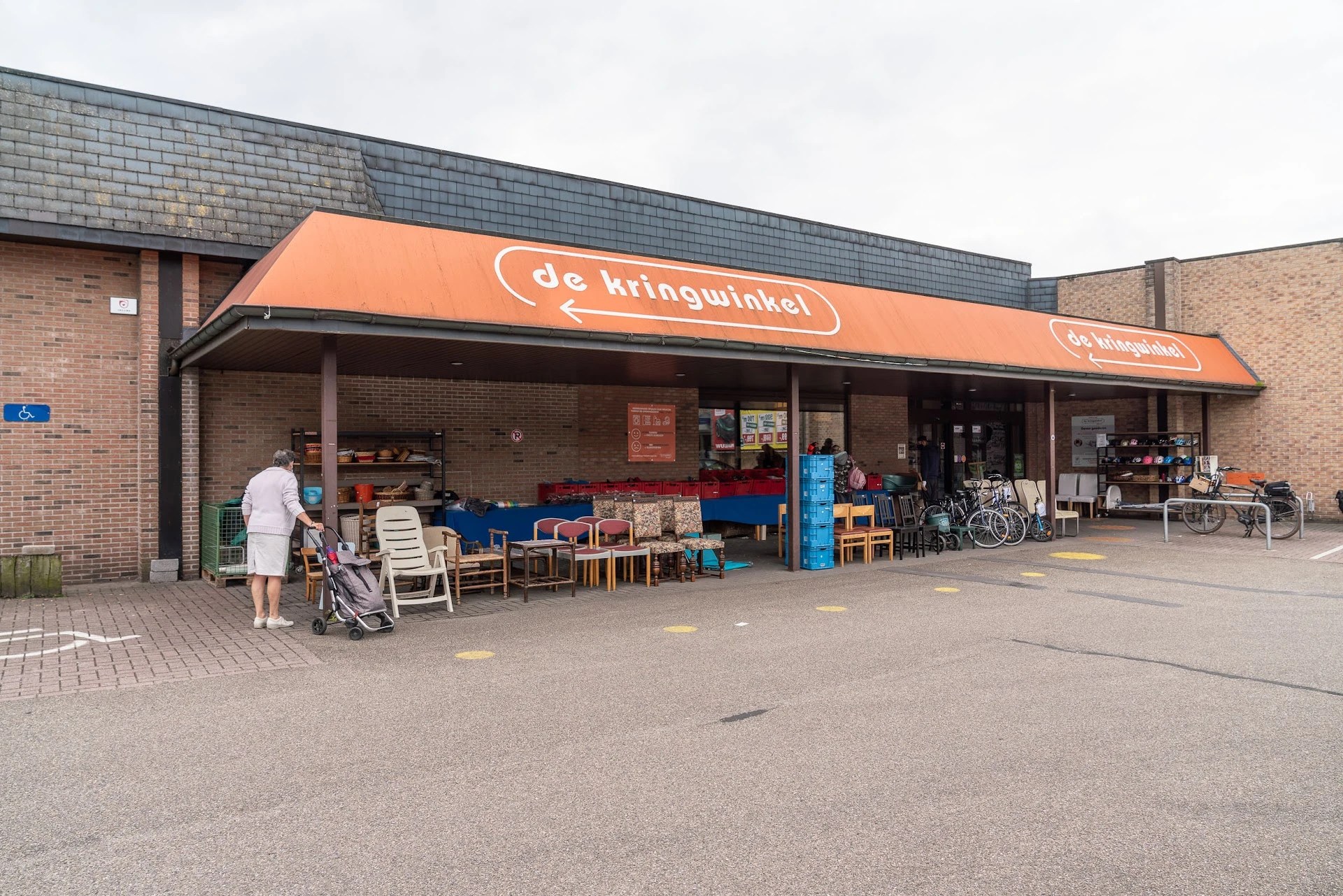 Voorgevel van kringloopwinkel met oranje luifel, uitgestalde meubels en fietsen op het terras