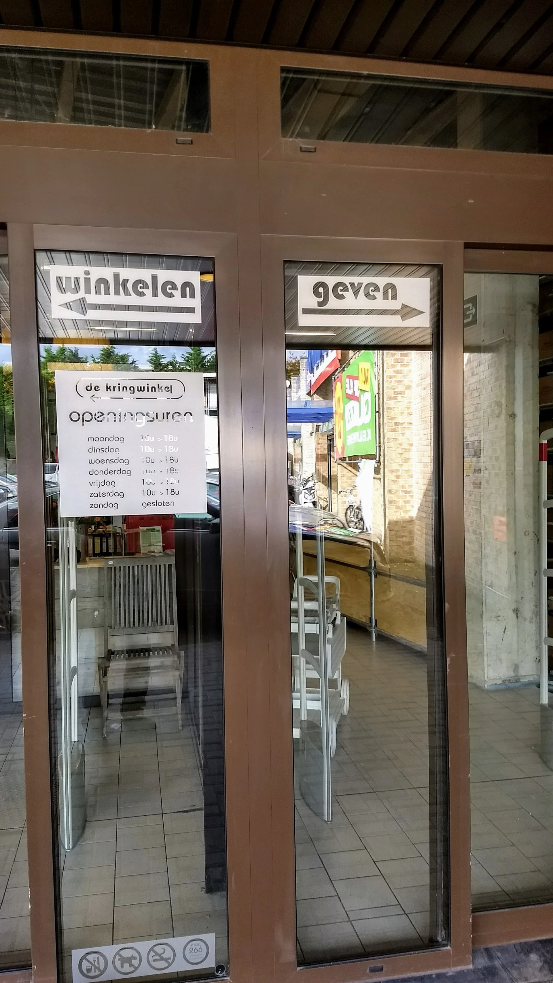Ingang van kringloopwinkel met glazen deuren en openingsuren op raam