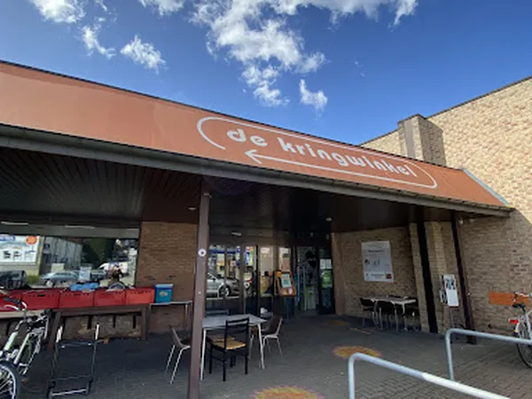 Gevel van kringloopwinkel met bruine luifel en naam 'de kringwinkel' zichtbaar, terras met stoelen ervoor