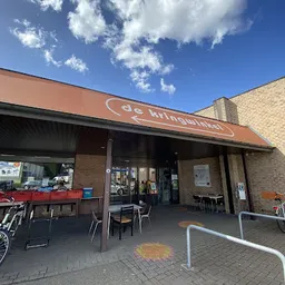 Gevel van kringloopwinkel met bruine luifel en naam 'de kringwinkel' zichtbaar, terras met stoelen ervoor