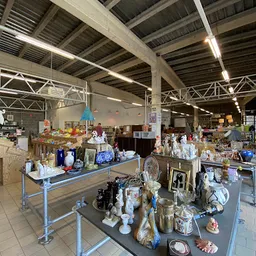 Overzicht van kringloopwinkelruimte met tafels vol decoratiespullen, servies en huishoudartikelen onder industrieel plafond