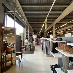 Winkelhal met stellingen vol kleding, schoenen en huishoudspullen langs het gangpad