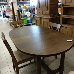 Ronde houten eettafel met uitschuifblad en bruine stoelen in kringloopwinkel