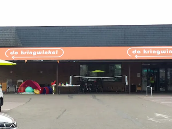 Voorgevel van kringloopwinkel met oranje luifel en naam 'de kringwinkel', speelgoed buiten uitgestald