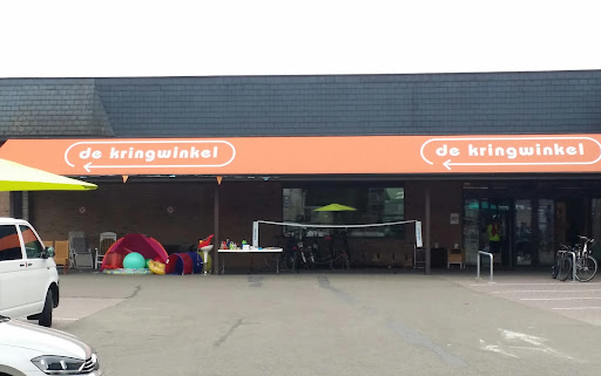 Voorgevel van kringloopwinkel met oranje luifel en naam 'de kringwinkel', speelgoed buiten uitgestald