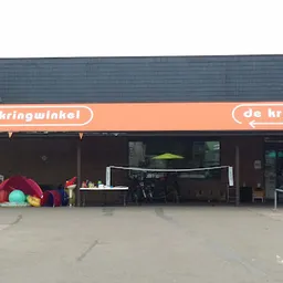 Voorgevel van kringloopwinkel met oranje luifel en naam 'de kringwinkel', speelgoed buiten uitgestald