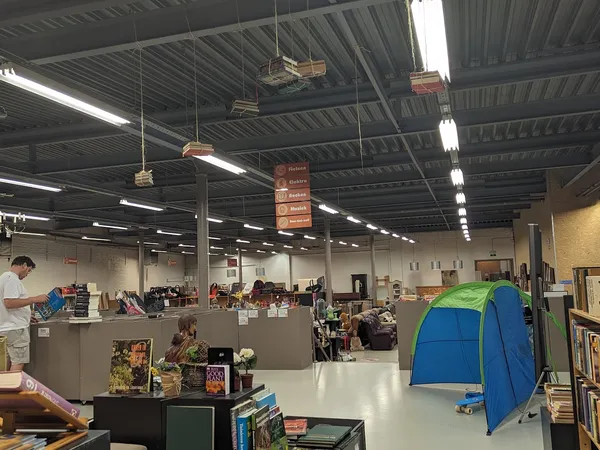 Ruime winkelhal met stellingen, toonbanken, opgehangen dozen en een blauwe pop-up tent, industrieel plafond met verlichtingel