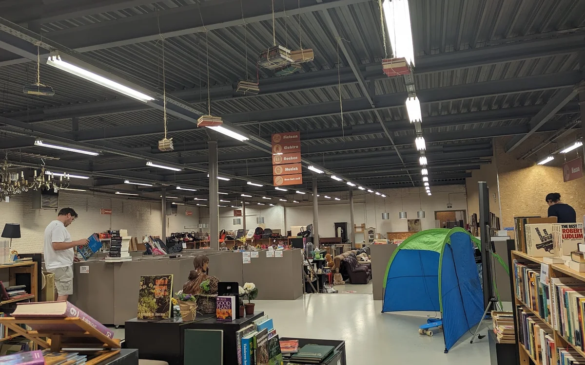 Ruime winkelhal met stellingen, toonbanken, opgehangen dozen en een blauwe pop-up tent, industrieel plafond met verlichtingel