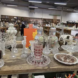 Uitgestalde kristallen vazen, schalen en decoratieve items op houten tafel in kringloopwinkel