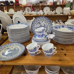 Uitgestalde blauwe en witte serviesgoed op houten tafel: stapels borden, kopjes en decoratieve schotels
