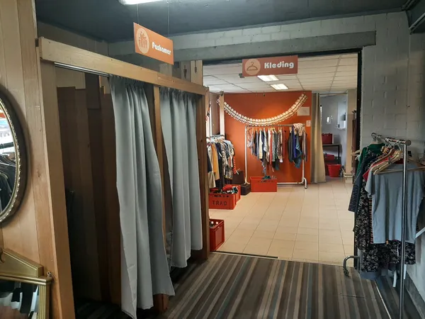 Winkelinterieur met kledingrekken, paskamers met grijze gordijnen en oranje decoratie in de achtergrond