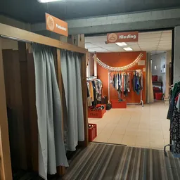 Winkelinterieur met kledingrekken, paskamers met grijze gordijnen en oranje decoratie in de achtergrond